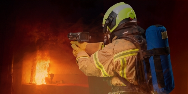 Palomies käyttää lämpökameraa taustalla näkyvää tulipaloa kuvaten.