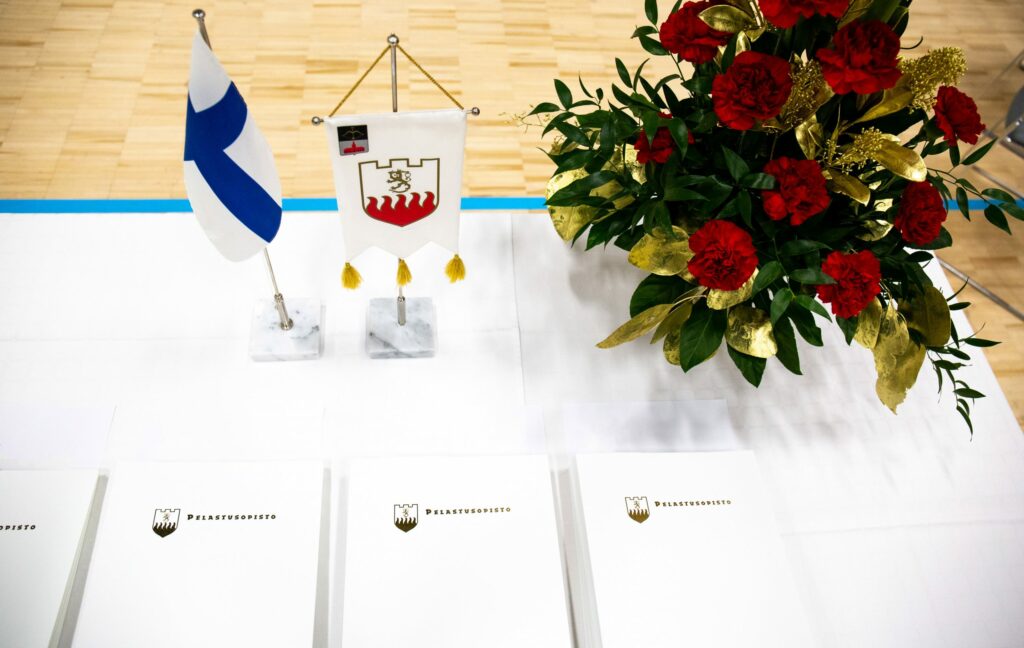 Juhlapöytä, jossa todistuksia, kukkakimppu, Pelastusopiston lippu ja Suomen lippu.