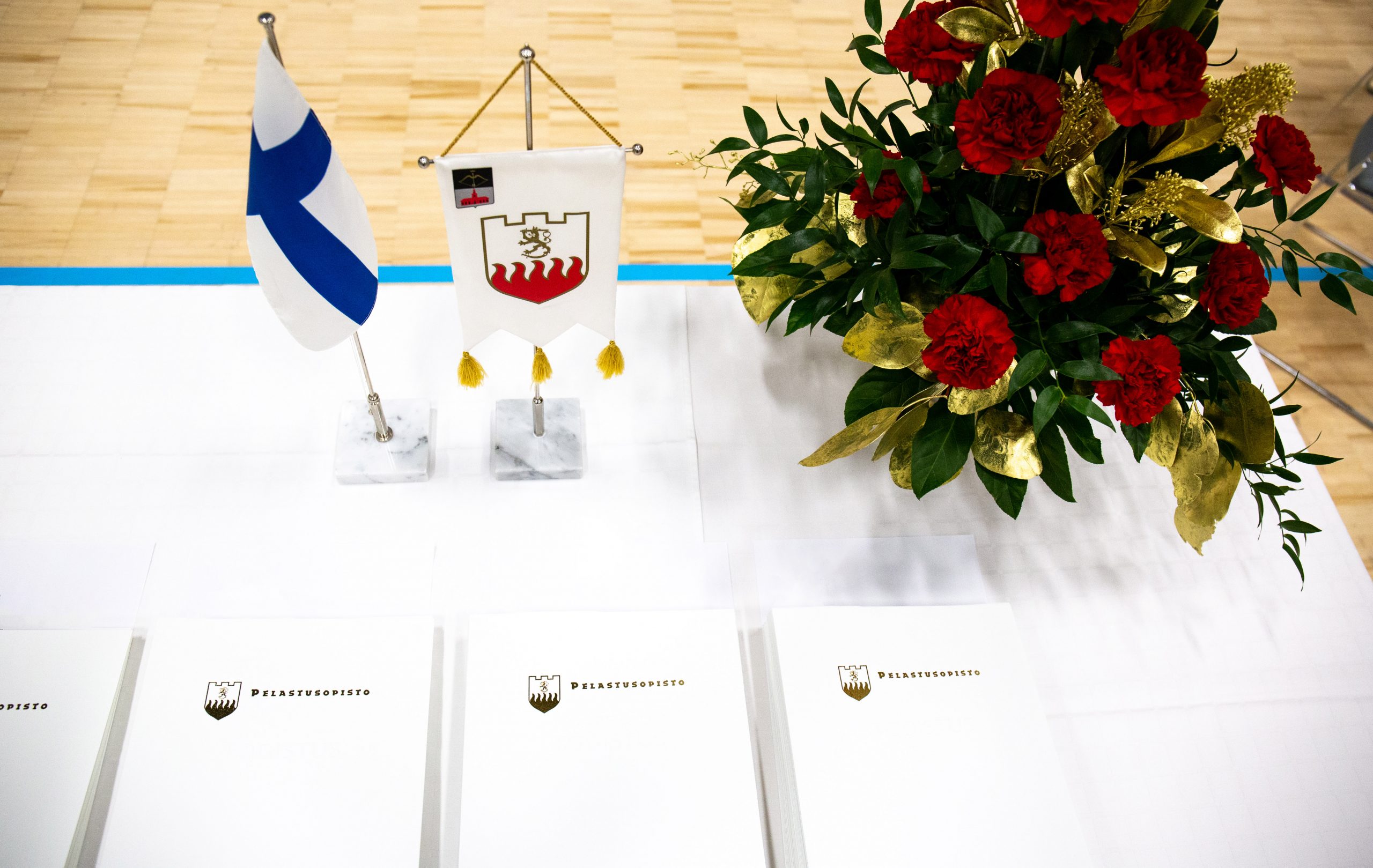 Juhlapöytä, jossa todistuksia, kukkakimppu, Pelastusopiston lippu ja Suomen lippu.