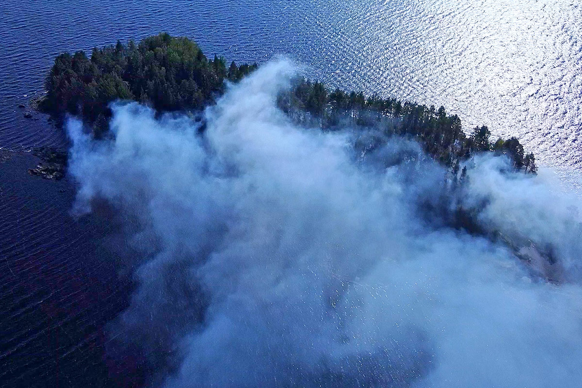 Ilmakuva saaresta, metsän keskeltä nousee sankka savu.