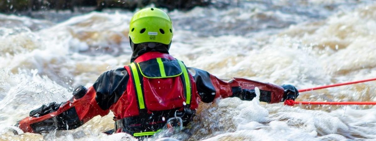 Pelastusasuinen henkilö kahlaa selin kameraan päin syvällä virtaavassa vedessä.