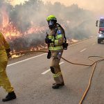 Kaksi pelastajaa ja sammutusauto tiellä, tien vieressä palaa tulipalo.