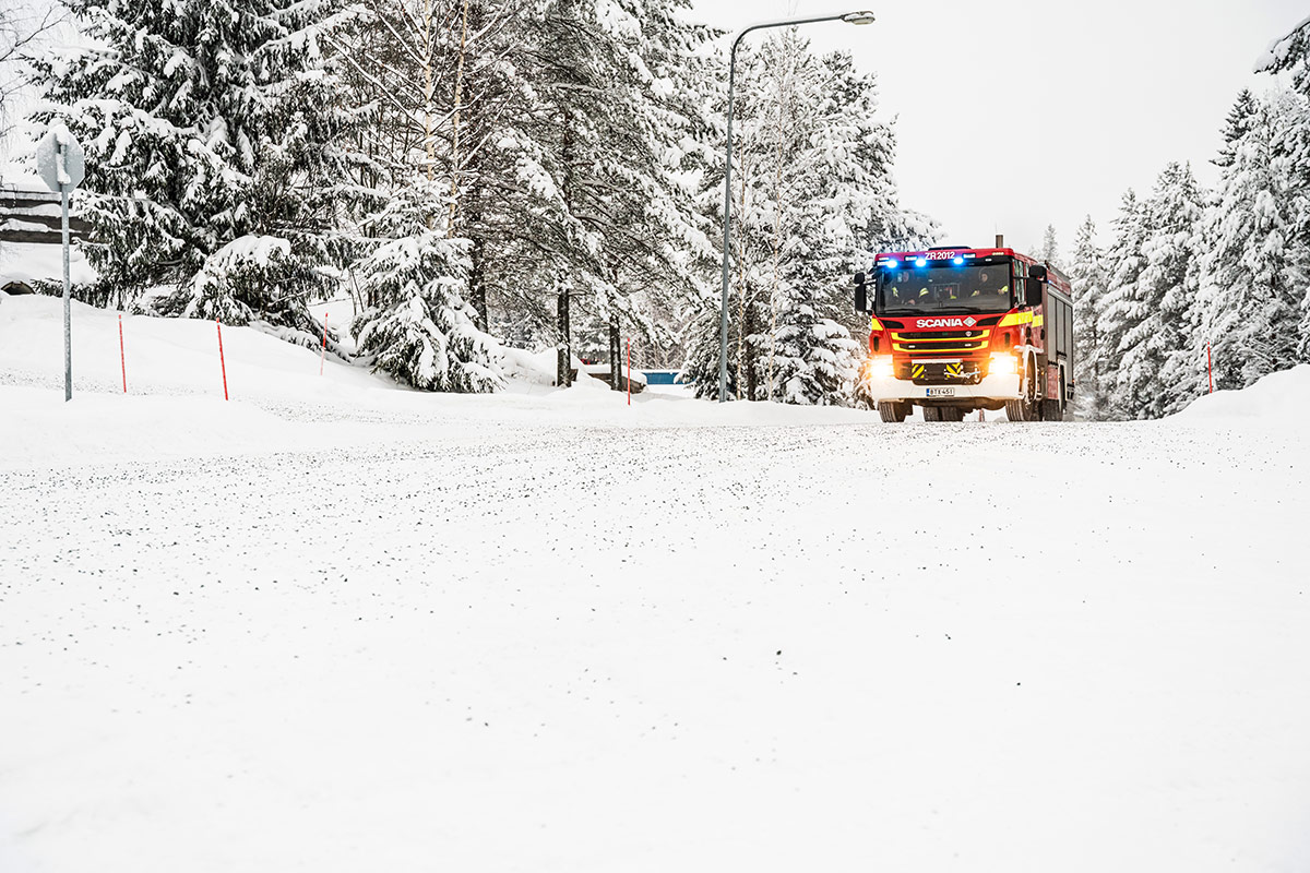 Talvinen maisema Pelastusopiston harjoitusalueella, tietä pitkin ajaa sammutusauto.