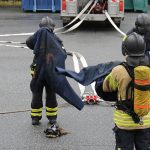 Pelastustoimen henkilöstöä sammutusasuissa, taustalla sammutusauto ja sammutusletkuja.