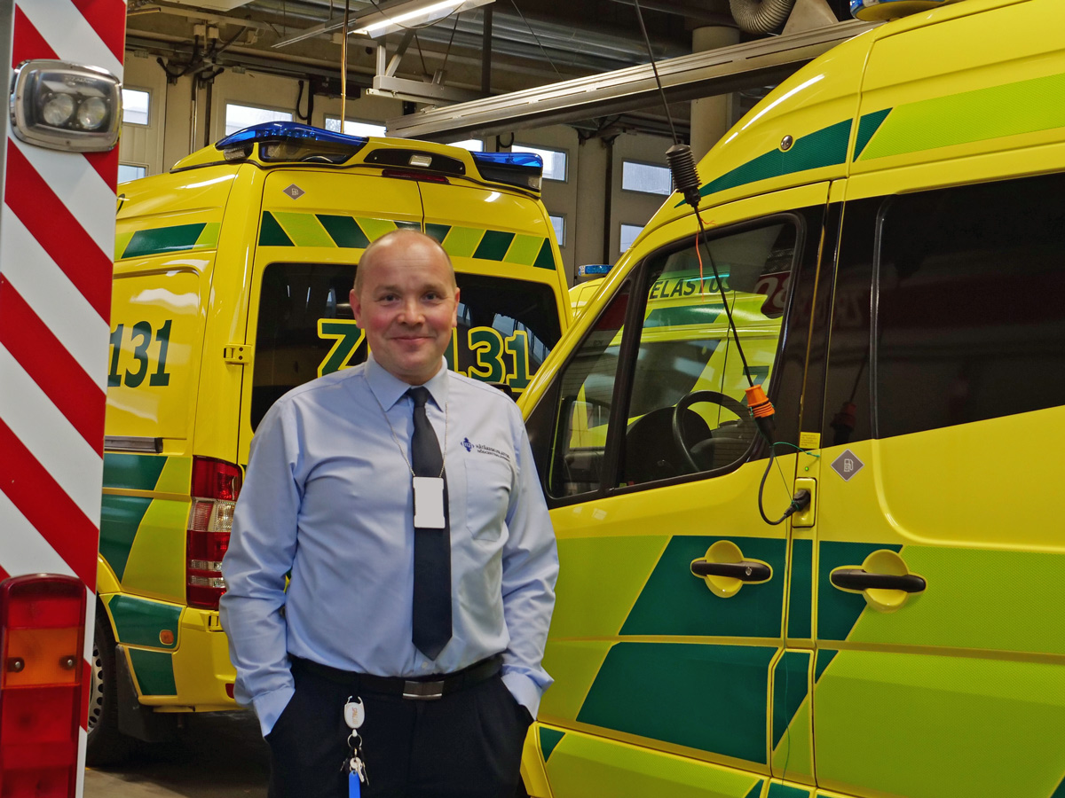 Jani seisoo opiskelijapuvussaan ambulanssien ja paloauton välissä kalustohallissa.