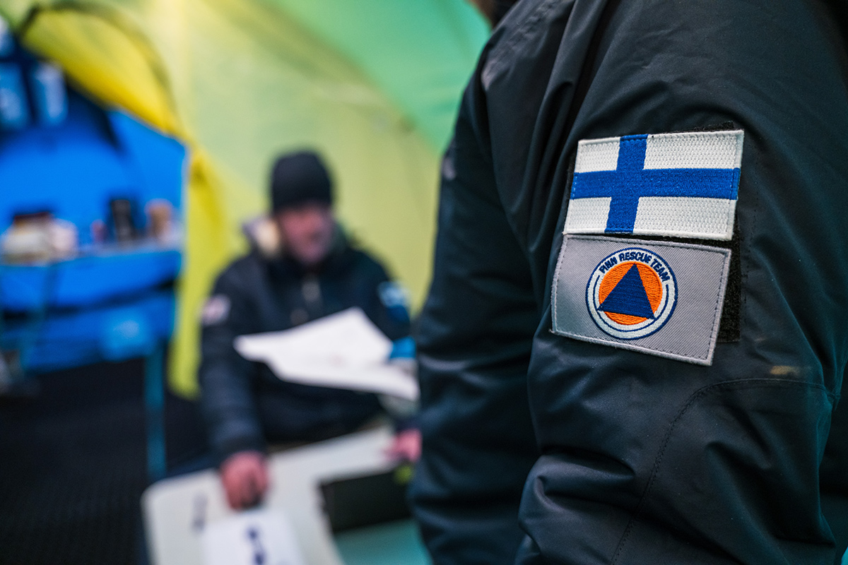 Finn Rescue Teamin telttaleirin vastaanotossa. Lähikuva takin hihasta, jossa Suomen lippu ja Finn Rescue Teamin logo.