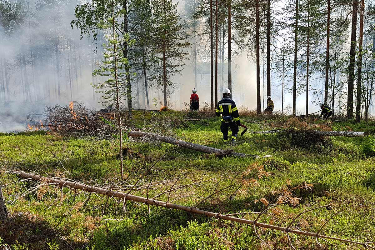 Henkilöitä seuraamassa paloa, savu nousee taivaalle.