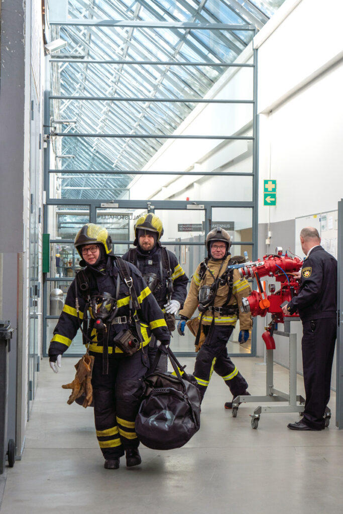 Sisäministeri Krista Mikkonen kantaa varustekassia sammutusvarusteisiin pukeutuneena.