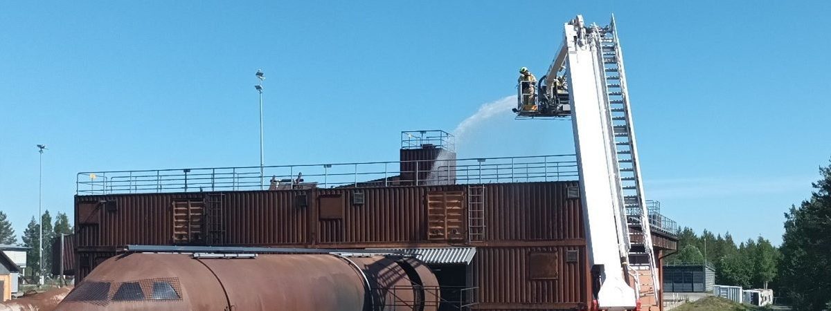 Nostolava-auton nostolavalta suihkutetaan vettä rakennuksen päälle.