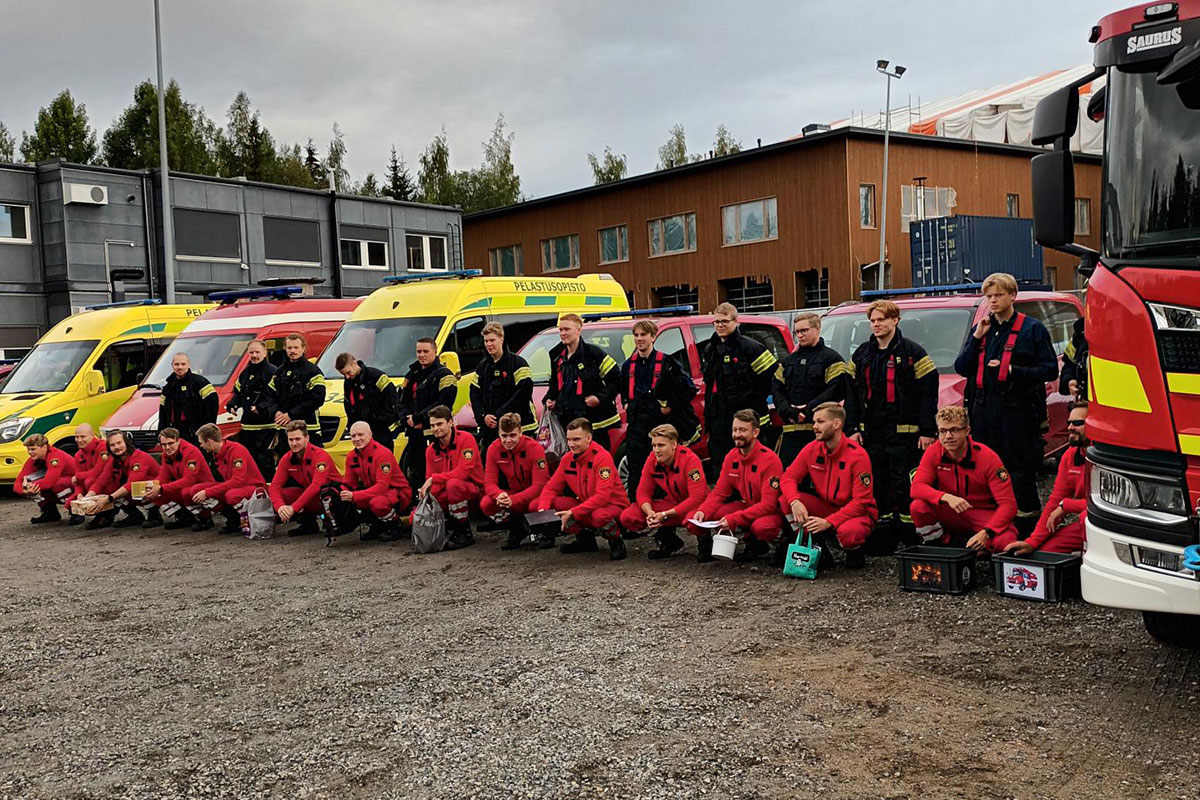 Ryhmäkuva pelastajaopiskelijoista, taustalla sammutusauto, ambulansseja ja muita ajoneuvoja.