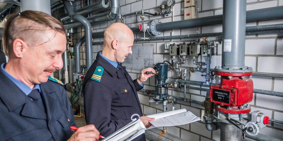 Kaksi virkapukuista henkilöä tutkii laitteita ja kirjaa havaintoja ylös.