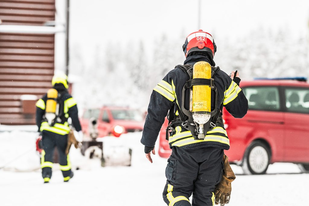 Talvinen maisema, kaksi pelastusasuista henkilöä kävelee ulkona, taustalla pelastustoimen punaisia autoja.