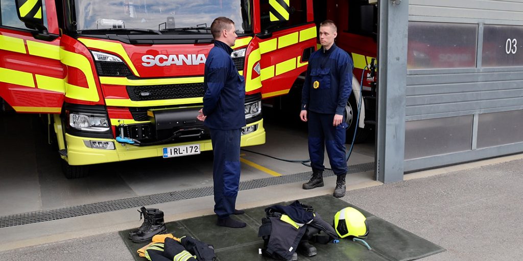 Kaksi kurssilaista kalustohallilla, sammutusauton edessä. Maassa sammutusvarusteet järjesteltynä.