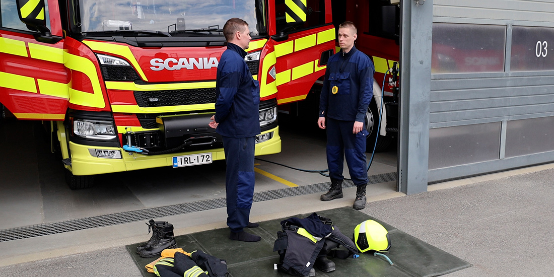 Kaksi kurssilaista kalustohallilla, sammutusauton edessä. Maassa sammutusvarusteet järjesteltynä.