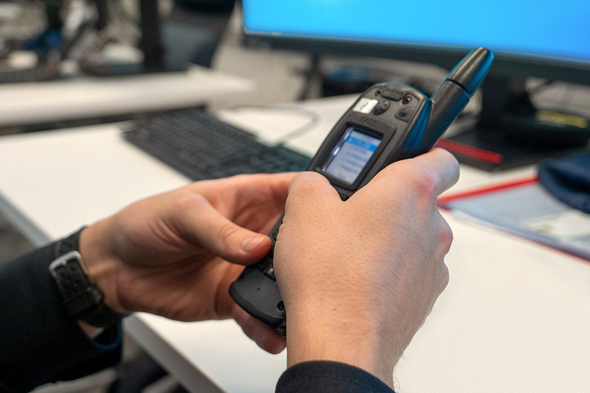 Pelastustoimen henkilö istuu työpöydän ääressä, henkilö pitää käsissään Virve-puhelinta.