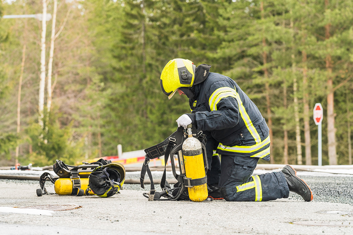 Sammutusasuinen henkilö tutkii kumartuneena maassa olevia varusteita.