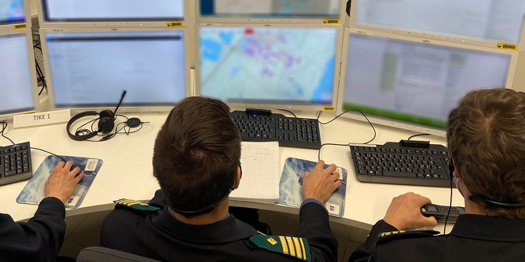 Pelastustoimen henkilöitä tietokonepöydän ääressä, edessä useita näyttöjä.