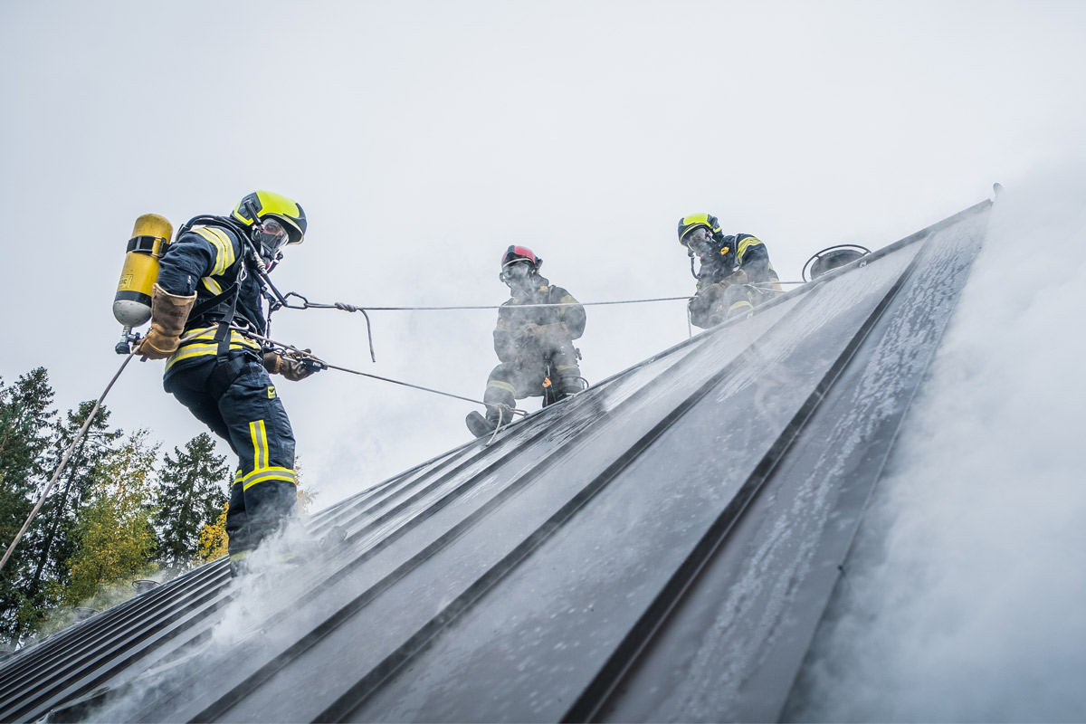 Pelastajatutkinnon opiskelijat harjoittelemassa kattotyöskentelyä. Yksi opiskelija laskeutuu köydellä ja kaksi muuta henkilöä varmistavat.