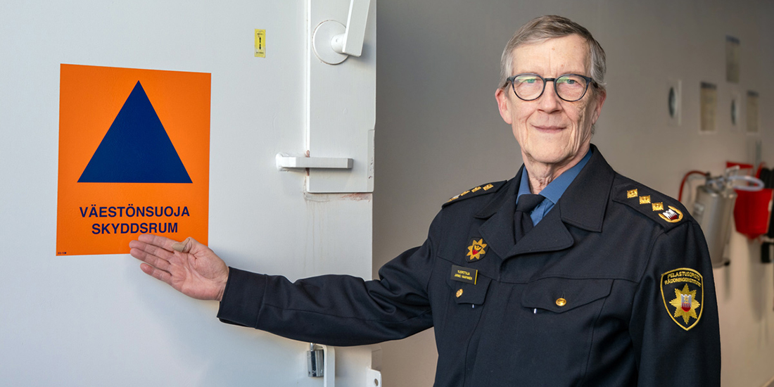 Pelastusopiston yliopettaja Jarmo Haapanen seisoo väestönsuojan ovella ja osoittaa oranssia väestönsuoja-merkkiä.