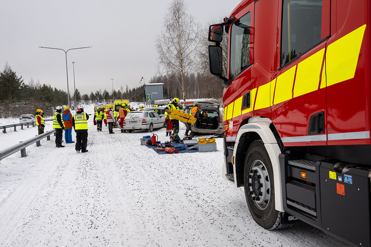 Suora tie, jonka varrella sammutusauto. Taustalla näkyy ambulansseja ja kolme liikenneonnettomuuteen joutunutta henkilöautoa. Paikalla paljon pelastushenkilöstöä.