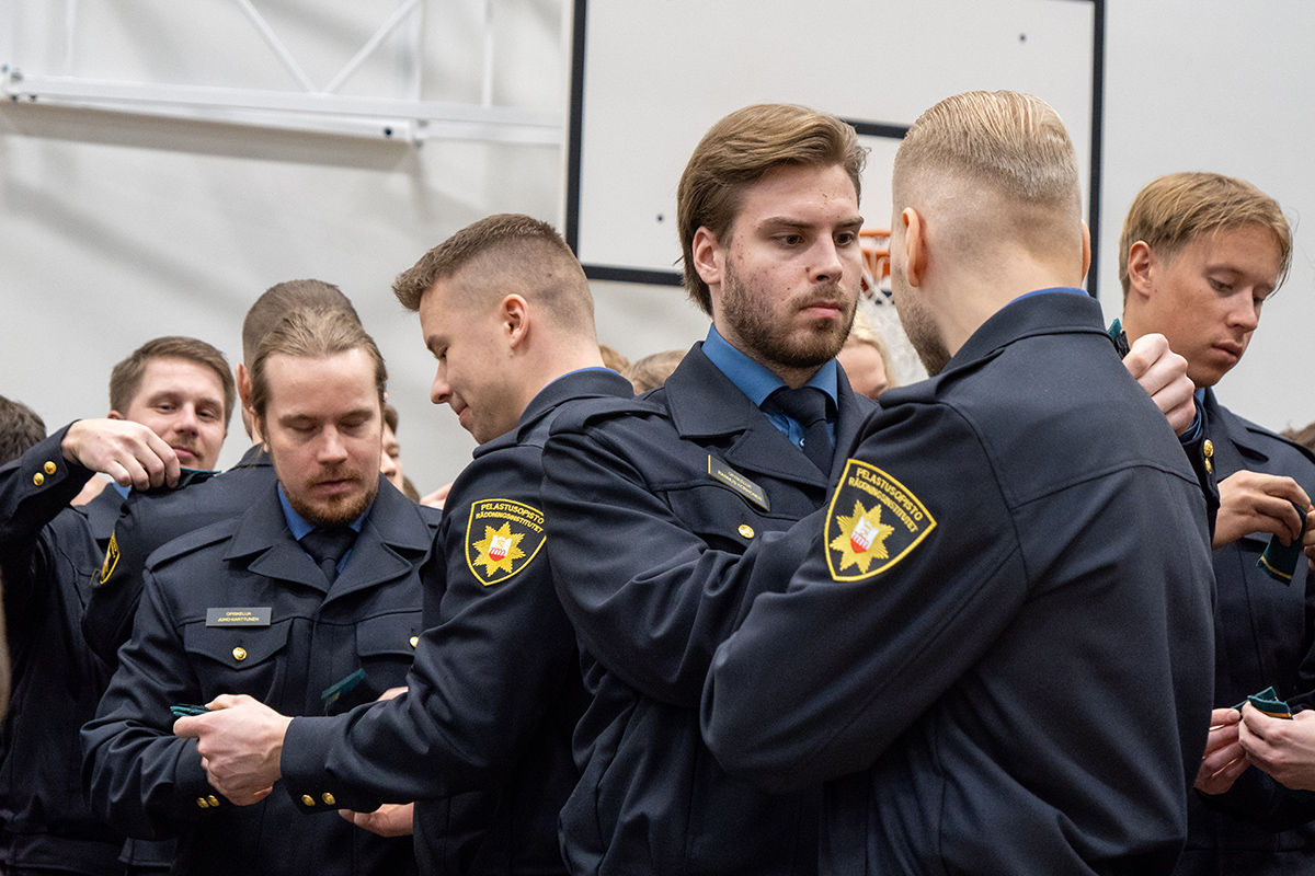 Aloittavat pelastajaopiskelijat kiinnittävät opiskelijatunnukset takkeihin.