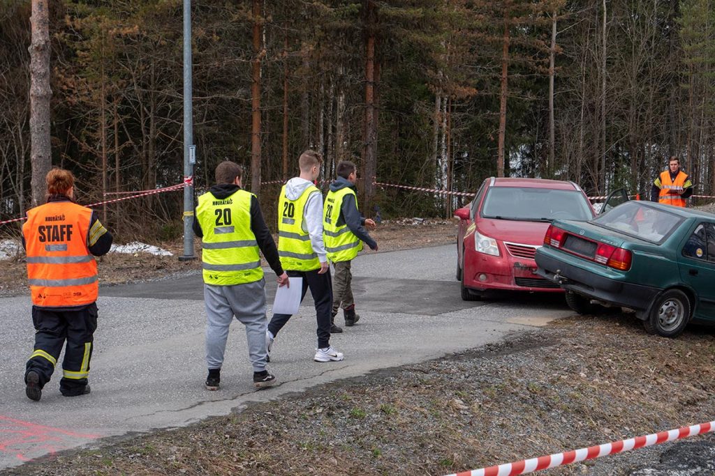 Kolmen hengen ryhmä kävelemässä harjoituspisteelle, mihin on järjestetty kahden auton kolari. Kaksi ohjaajaa seuraa ryhmän suoritusta.