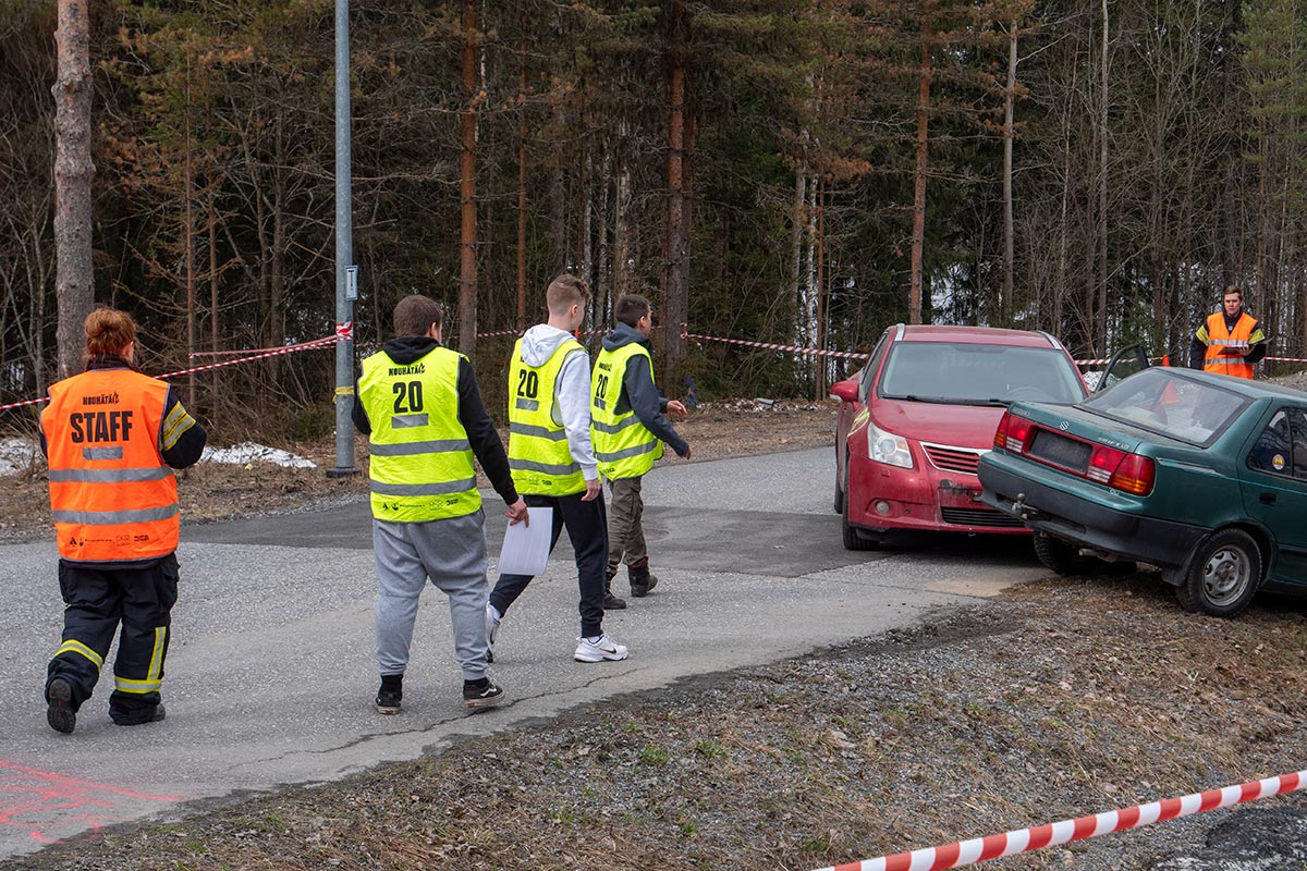 Kolmen hengen ryhmä kävelemässä harjoituspisteelle, mihin on järjestetty kahden auton kolari. Kaksi ohjaajaa seuraa ryhmän suoritusta.