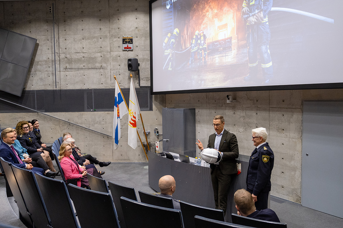Tasavallan presidentti ja Pelastusopiston rehtori auditorion edessä, rehtori luovutti presidentille priimuskypärän.