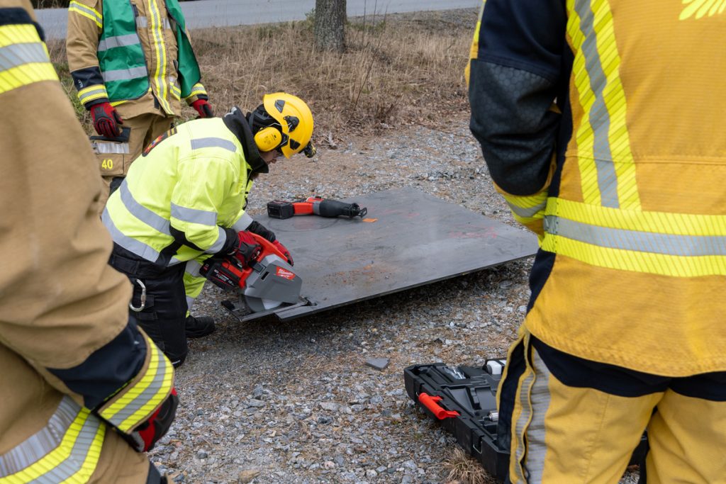Pelastustoimen henkilö leikkaa metallilevyä, ympärillä näkyy muita pelastustoimen henkilöitä.