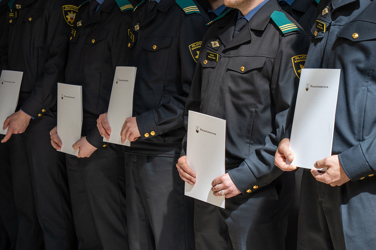 Valmistuneita pelastajaopiskelijoita seisoo rivissä käsissään tutkintotodistukset.