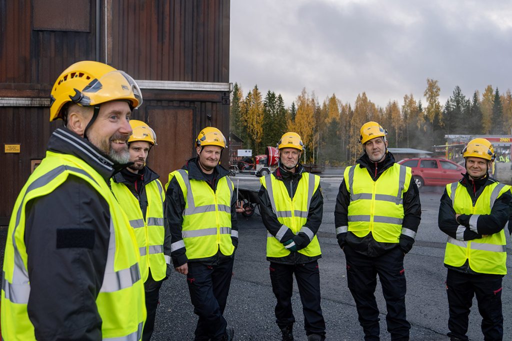 Ryhmä pelastusryhmäjohtajia seisoo turvaliivit ja kypärät yllään Pelastusopiston harjoitusalueella.