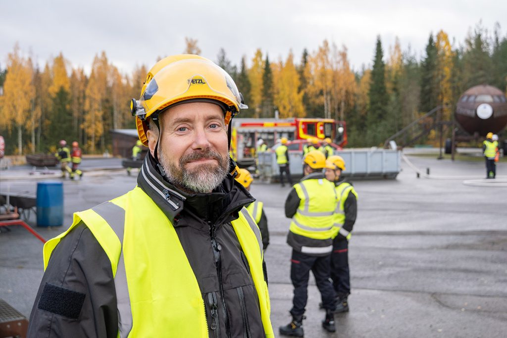 Pelastusopiston vanhempi opettaja Vesa Kujanpää Pelastusopiston harjoitusalueella, takanaan pelastusryhmänjohtajia.