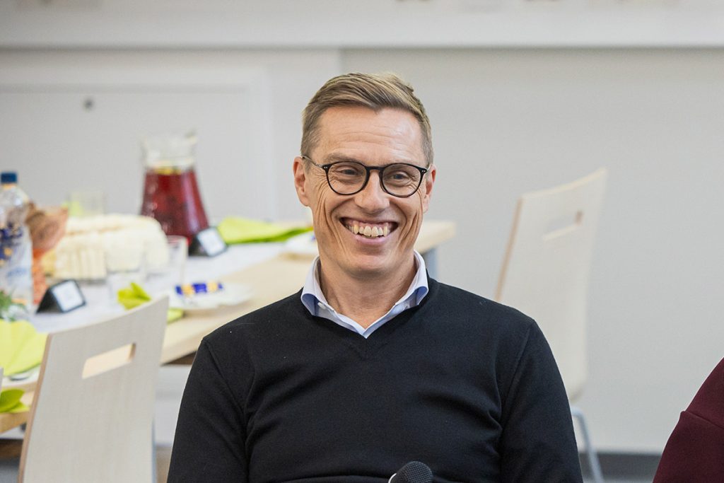 Tasavallan presidentti istuu pöydän ääressä ja hymyilee.