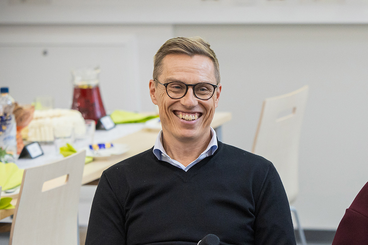 Tasavallan presidentti istuu pöydän ääressä ja hymyilee.